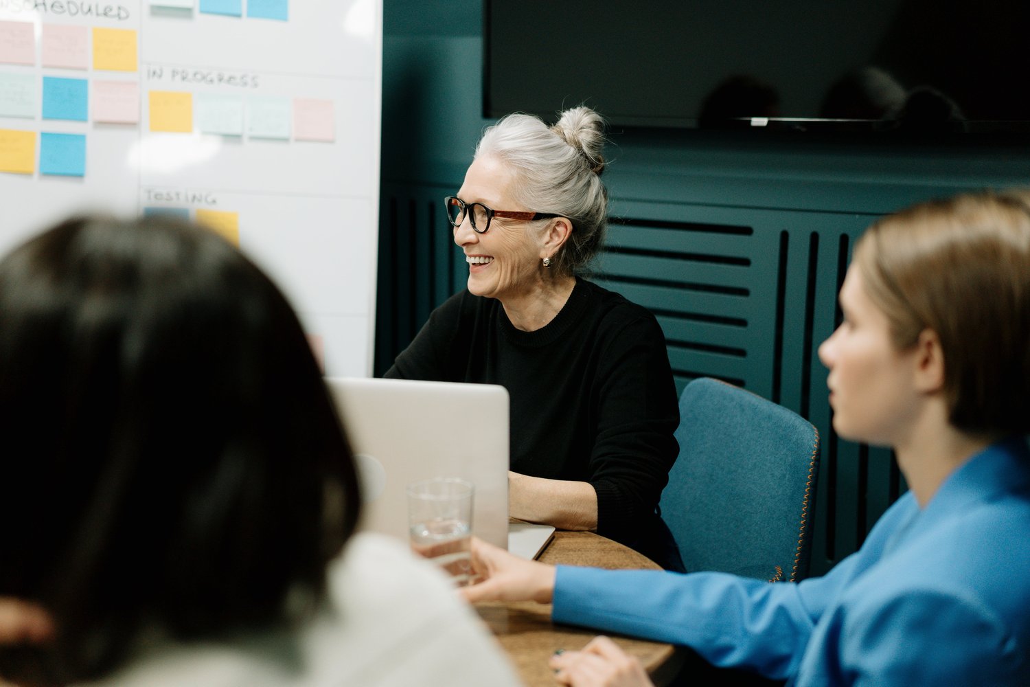 A woman in glasses sits at a table, smiling at her peers in an idea workshop.